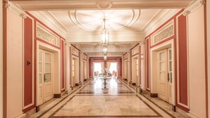 En lång, elegant hall med ett marmorgolv, en stor kristallkrona i mitten och dörrar på båda sidor som leder in till rummen.