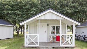 A small, single-story cabin with a porch, a door marked with the number 13, and a table with chairs outside. - First Camp Malmö (Malmö)