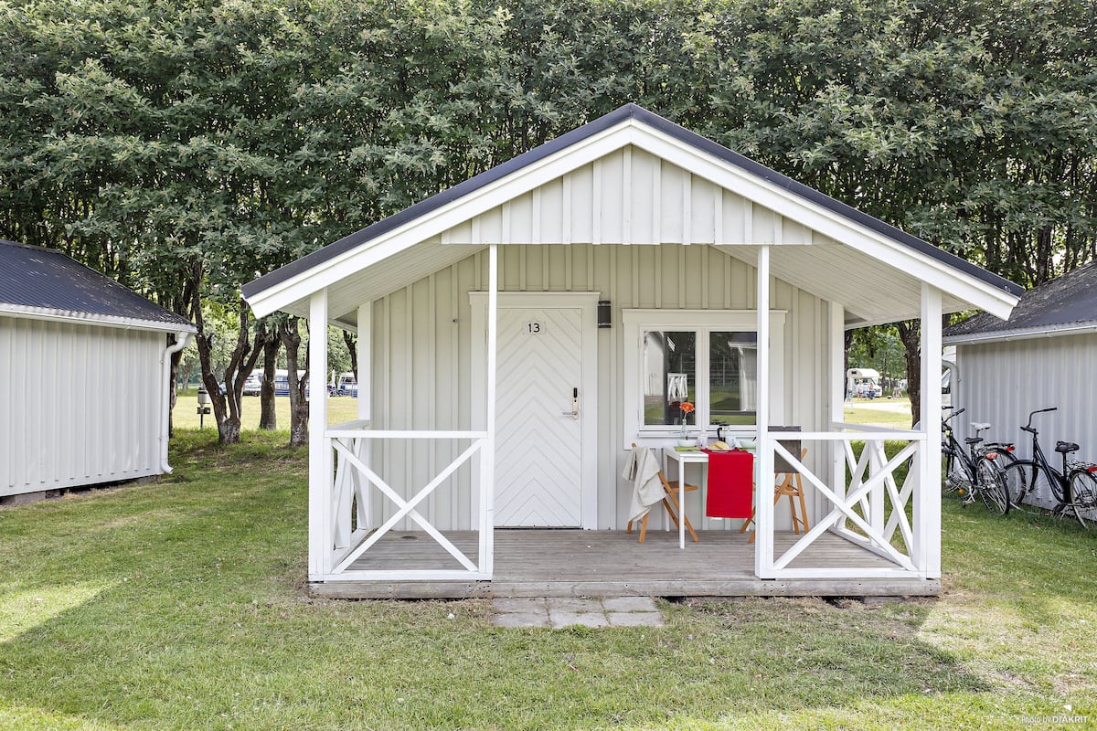 A small, single-story cabin with a porch, a door marked with the number 13, and a table with chairs outside.