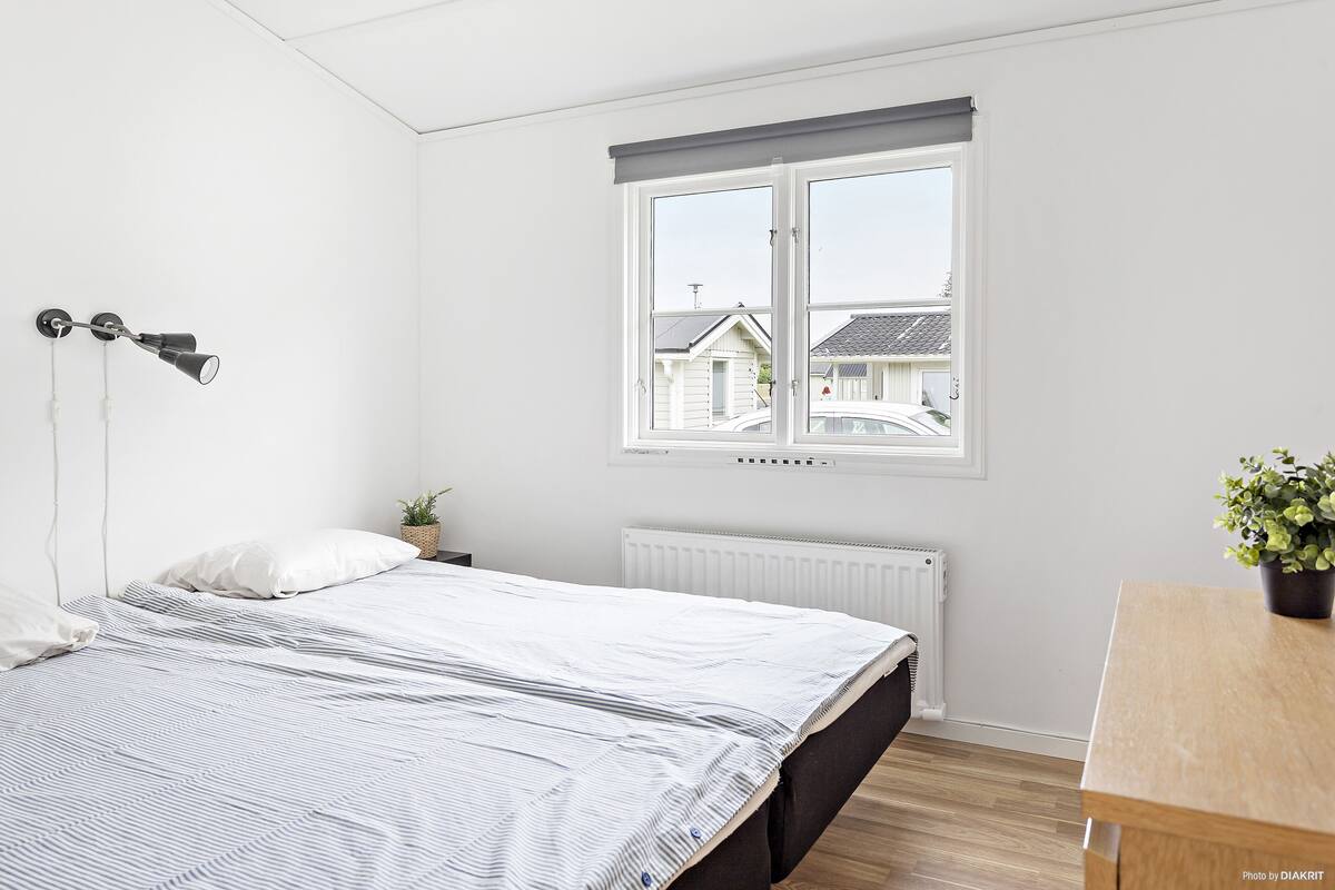 A bedroom with a bed, a window, a radiator, a bedside table, and a lamp.