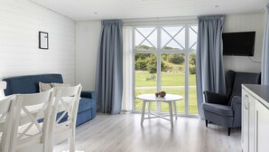 A room with a blue sofa, white chairs, a small round table, a grey armchair, and a TV mounted on the wall. - First Camp Malmö (Malmö)