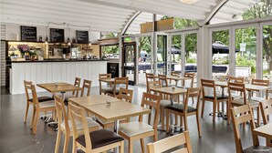 A modern cafe with wooden tables and chairs, a counter with a menu, and large windows offering a view of the outdoors. - First Camp Malmö (Malmö)