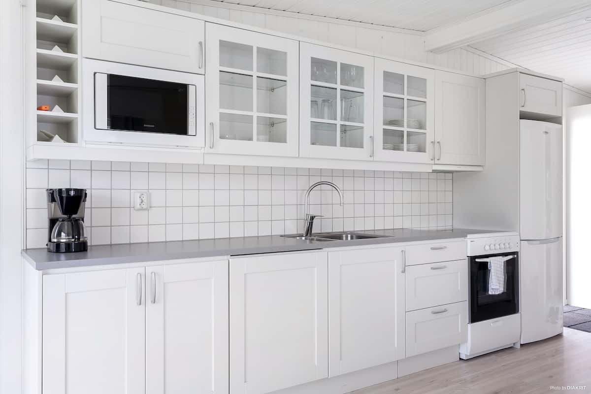 A modern kitchen with white cabinetry, a built-in microwave, a coffee maker, and a stove.