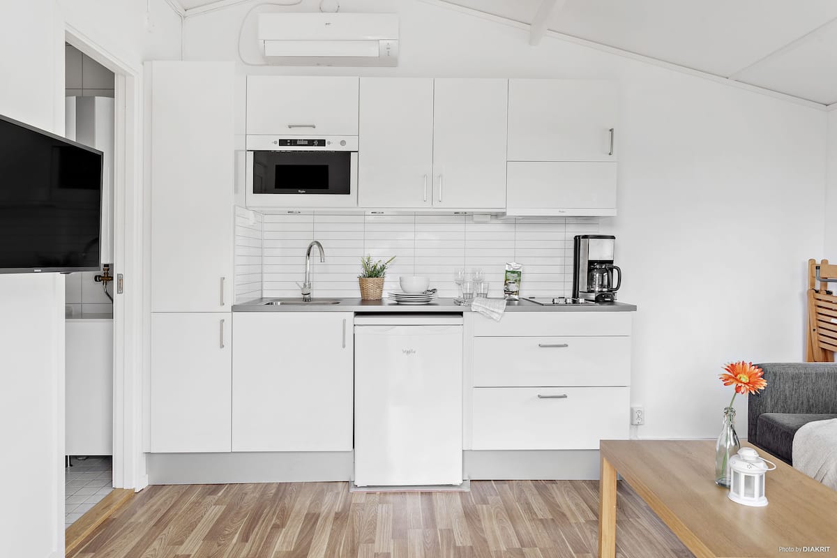 A modern kitchen with white cabinetry, a built-in microwave, a dishwasher, and a coffee maker.