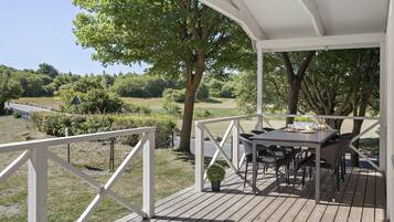 Une terrasse en bois avec une table et des chaises, entourée de rampes blanches et d’arbres.