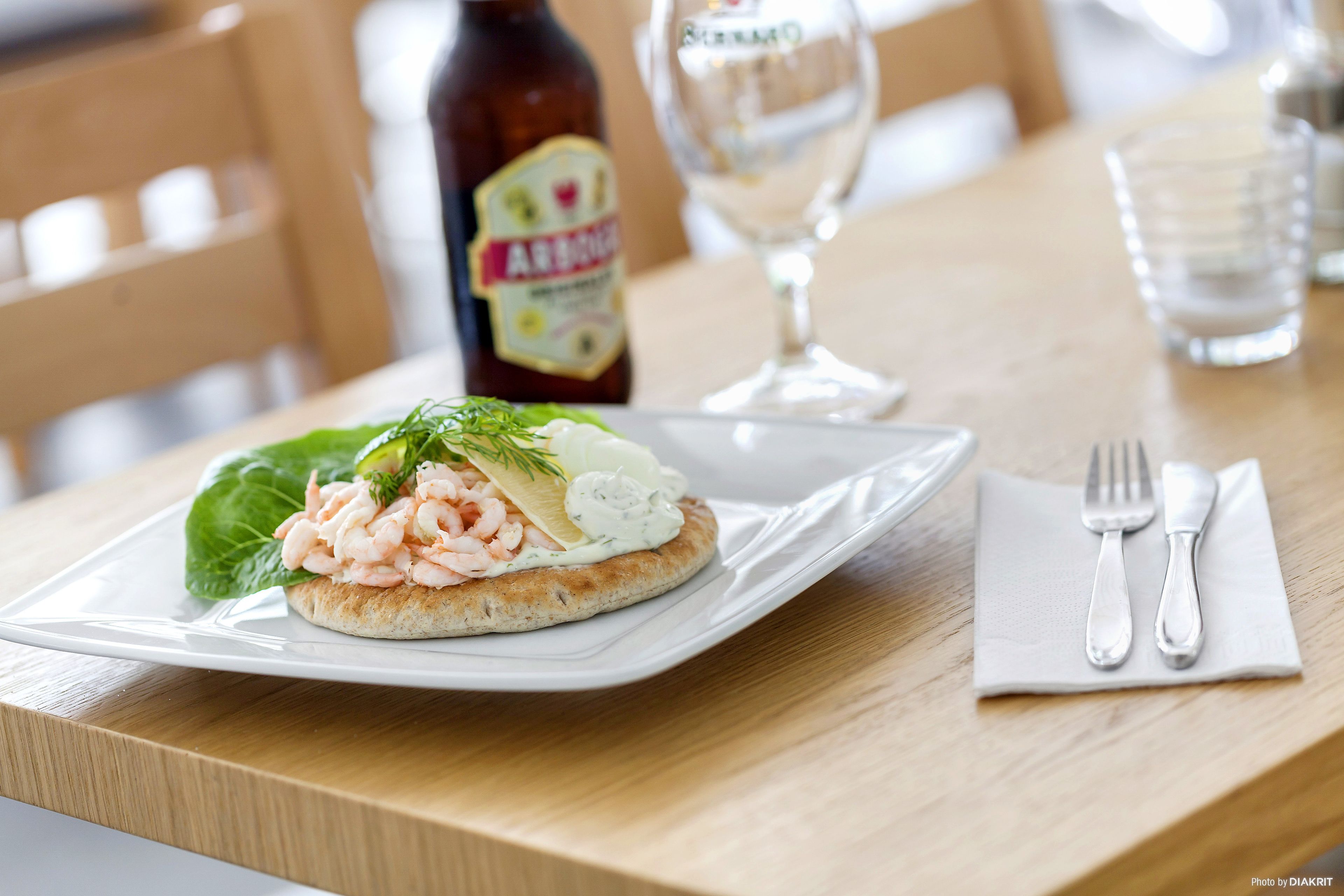 A plate with shrimp and a sauce on a cracker, a bottle of beer, and a glass of wine on a wooden table.