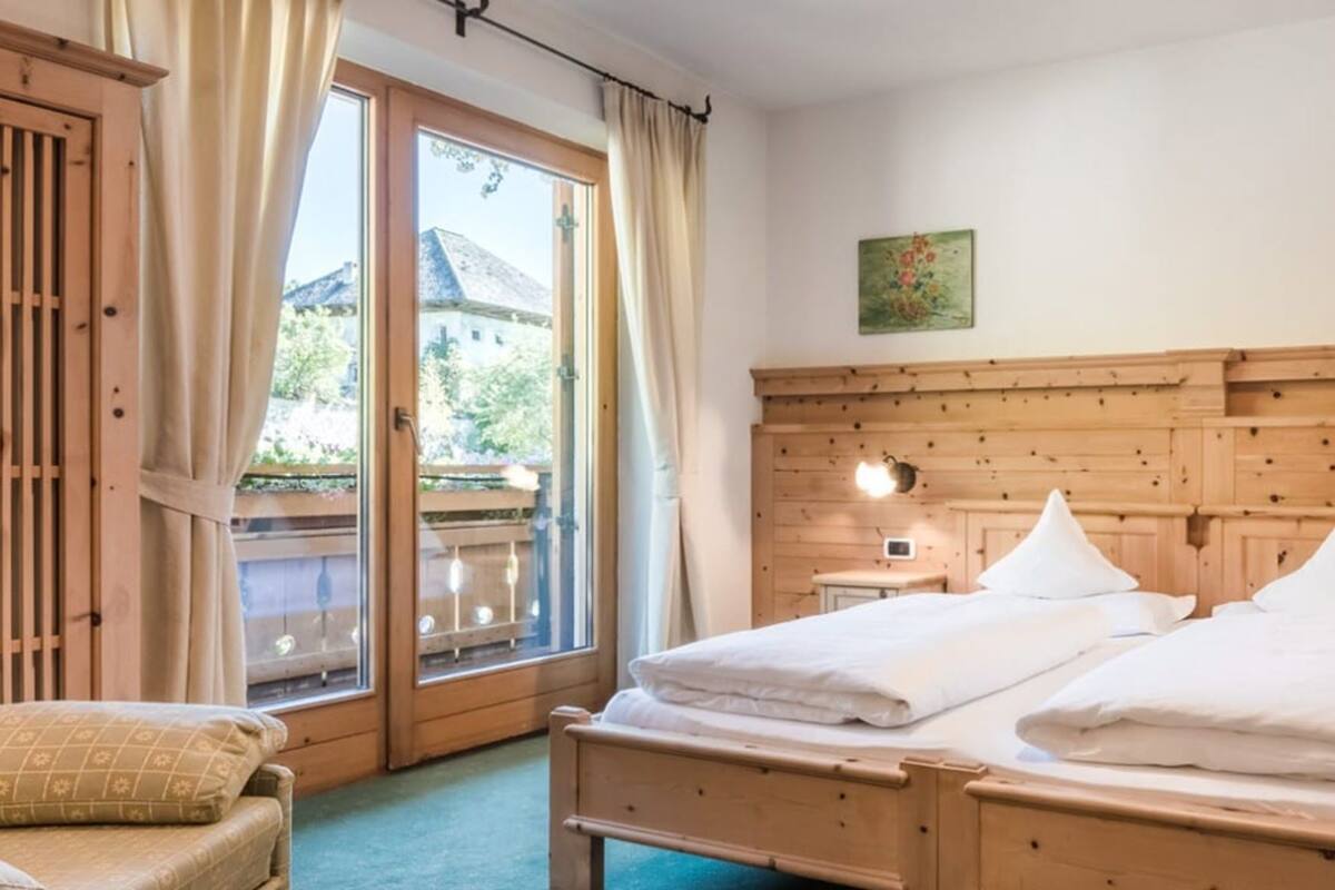 Un dormitorio de madera con una cama, dos mesitas de noche, una silla y una ventana con cortinas.