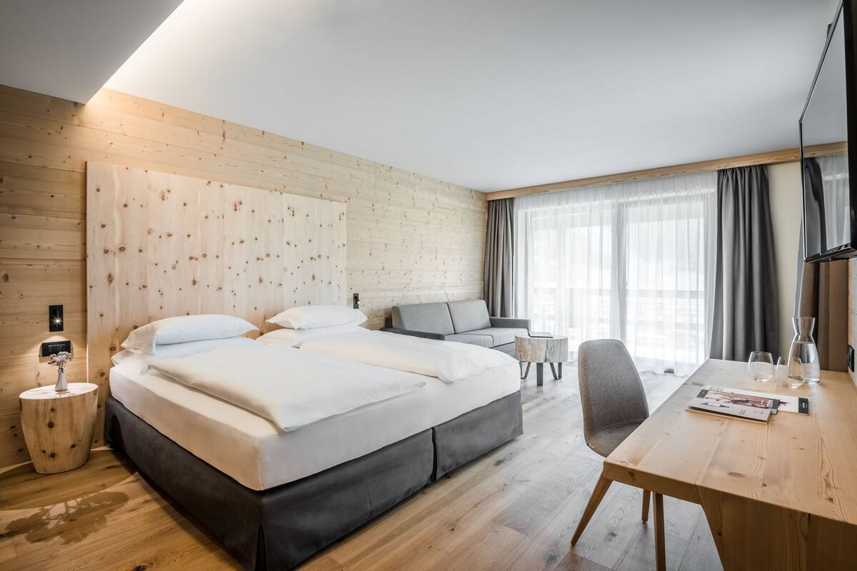 Habitación de hotel moderna con una cama grande, un escritorio y una silla. Se observa una ventana con cortinas y una pared de madera.