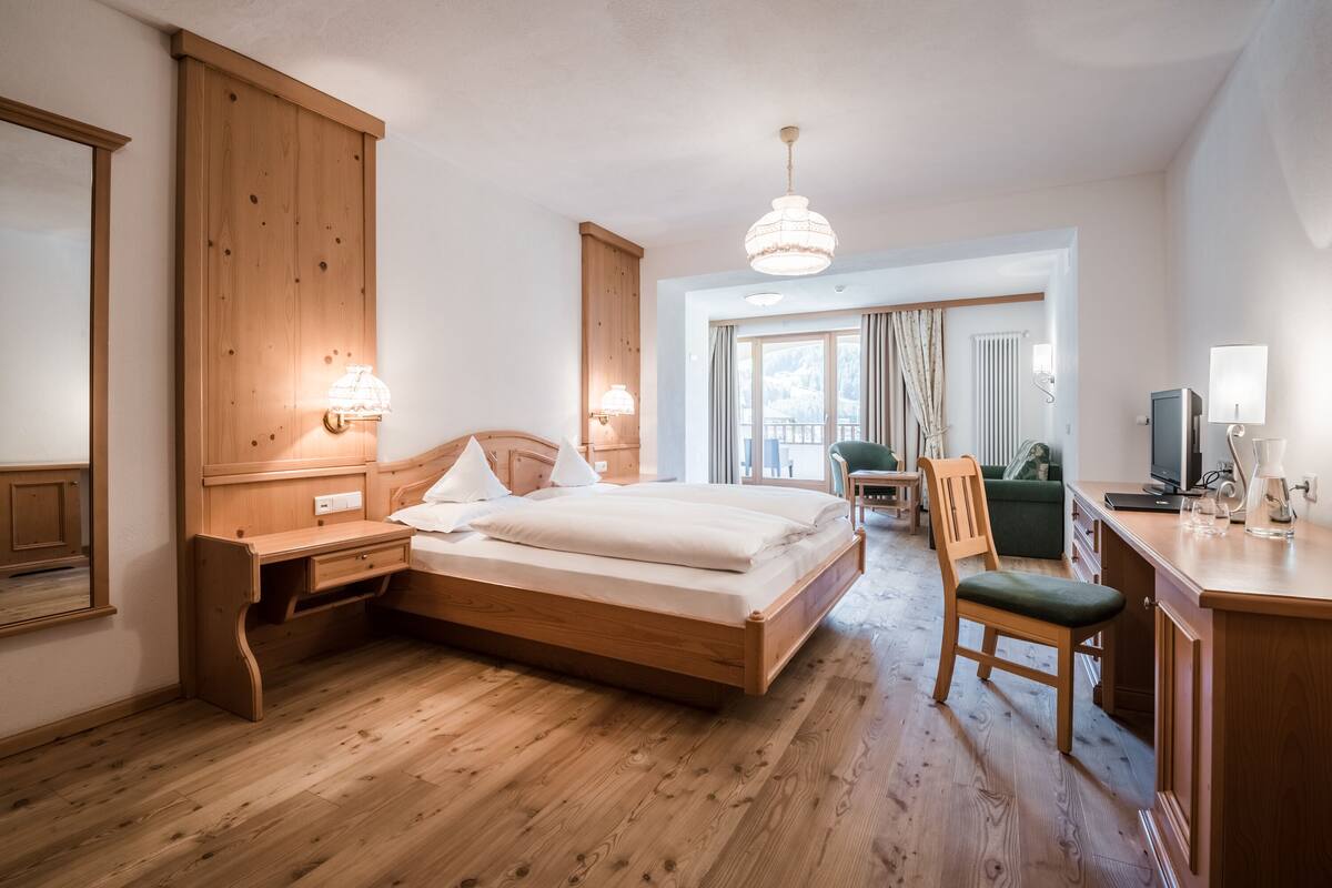Habitación de hotel con cama de madera, mesitas de noche, un escritorio, una silla y vistas a un balcón.