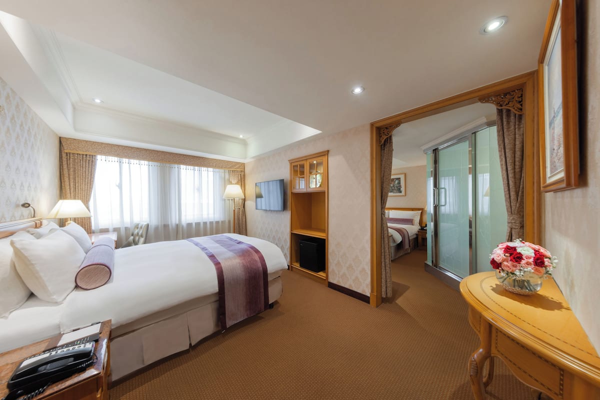 A hotel room with a bed, bedside table, lamp, and a small table with a vase of flowers.
