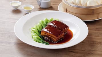 A plate with a glazed meat dish, bok choy, and a wooden steamer with dumplings.