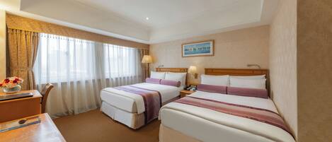 A hotel room with two beds, a desk, and a chair. There is a painting on the wall and a window with curtains.