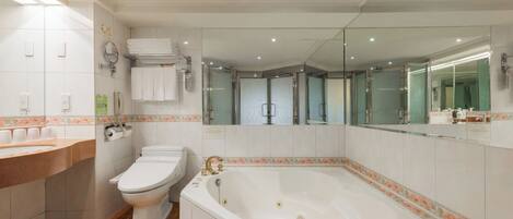 A modern bathroom with a white toilet, a large bathtub, a sink with a mirror, and a shower area.