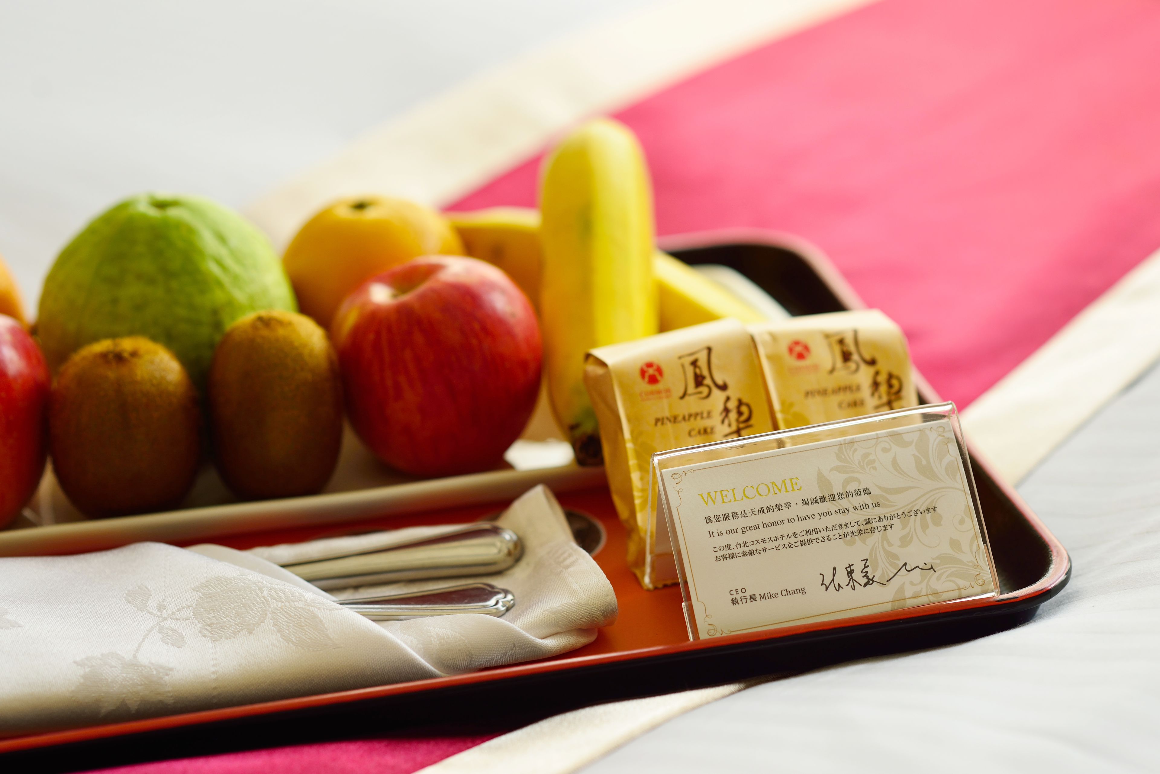 A tray with fruits, a napkin, and a welcome card on a table.