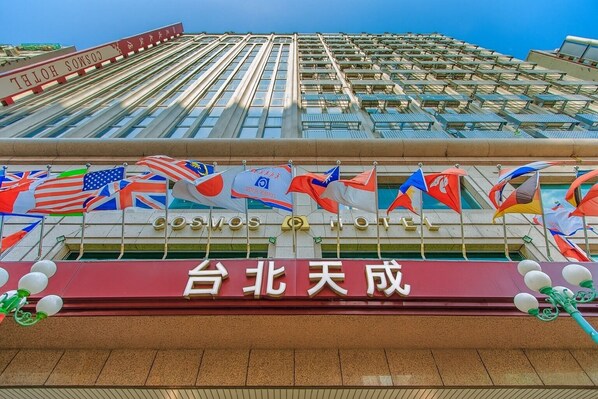 A hotel with a prominent sign reading "COSMOS HOTEL" and a banner with Chinese characters. Flags of various countries are displayed in front of the building. - Cosmos Hotel Taipei (Taipei)