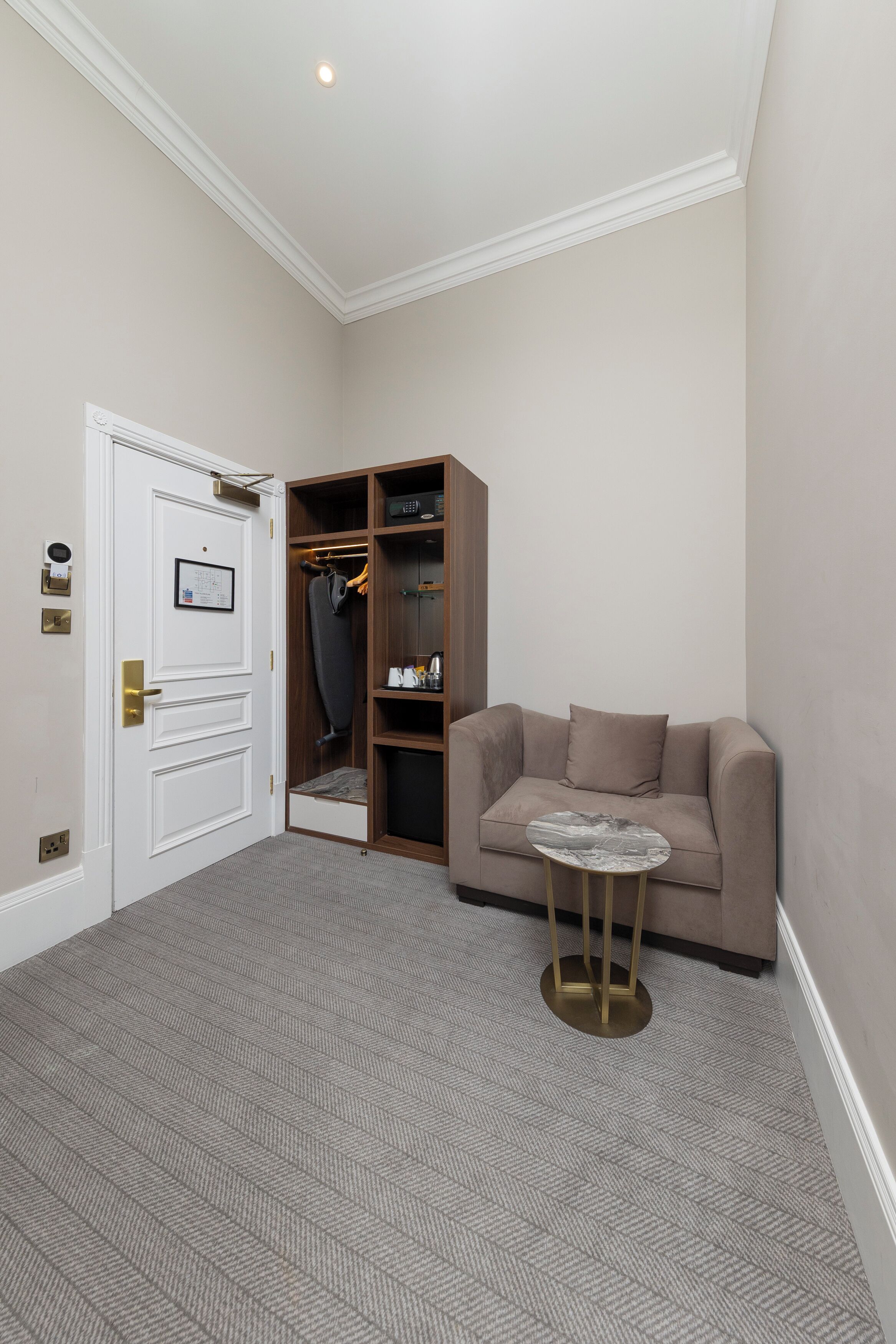 A room with a beige carpet, a beige sofa, a small round table, and a wooden wardrobe with a mirror.