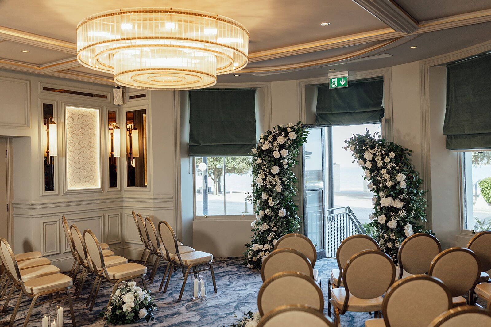 Un salón de conferencias con candelabro, sillas, suelo alfombrado y un arreglo floral cerca de la entrada.