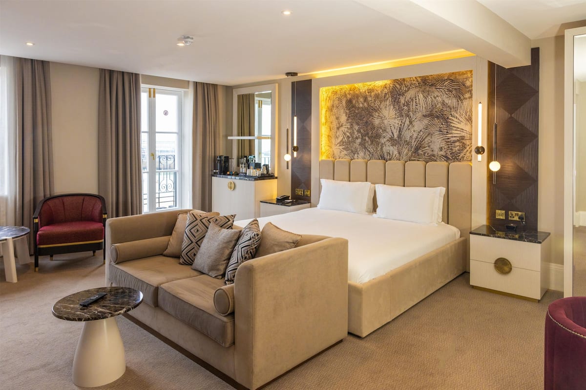 A hotel room with a bed, a sofa, a small table, a nightstand, and a chair.