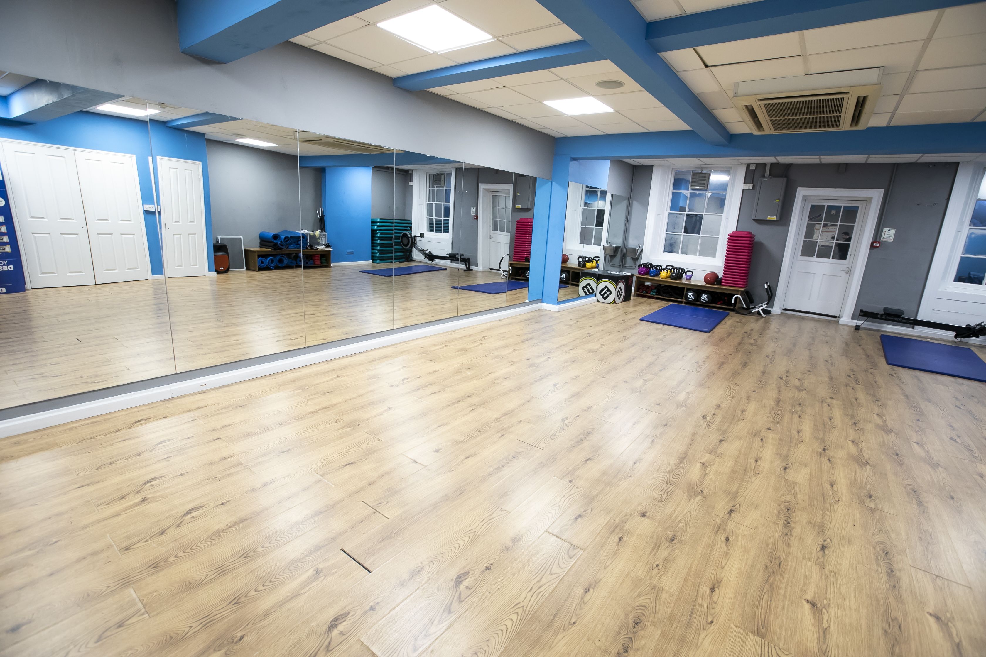 A spacious gym with wooden floors, mirrored walls, and various exercise equipment.