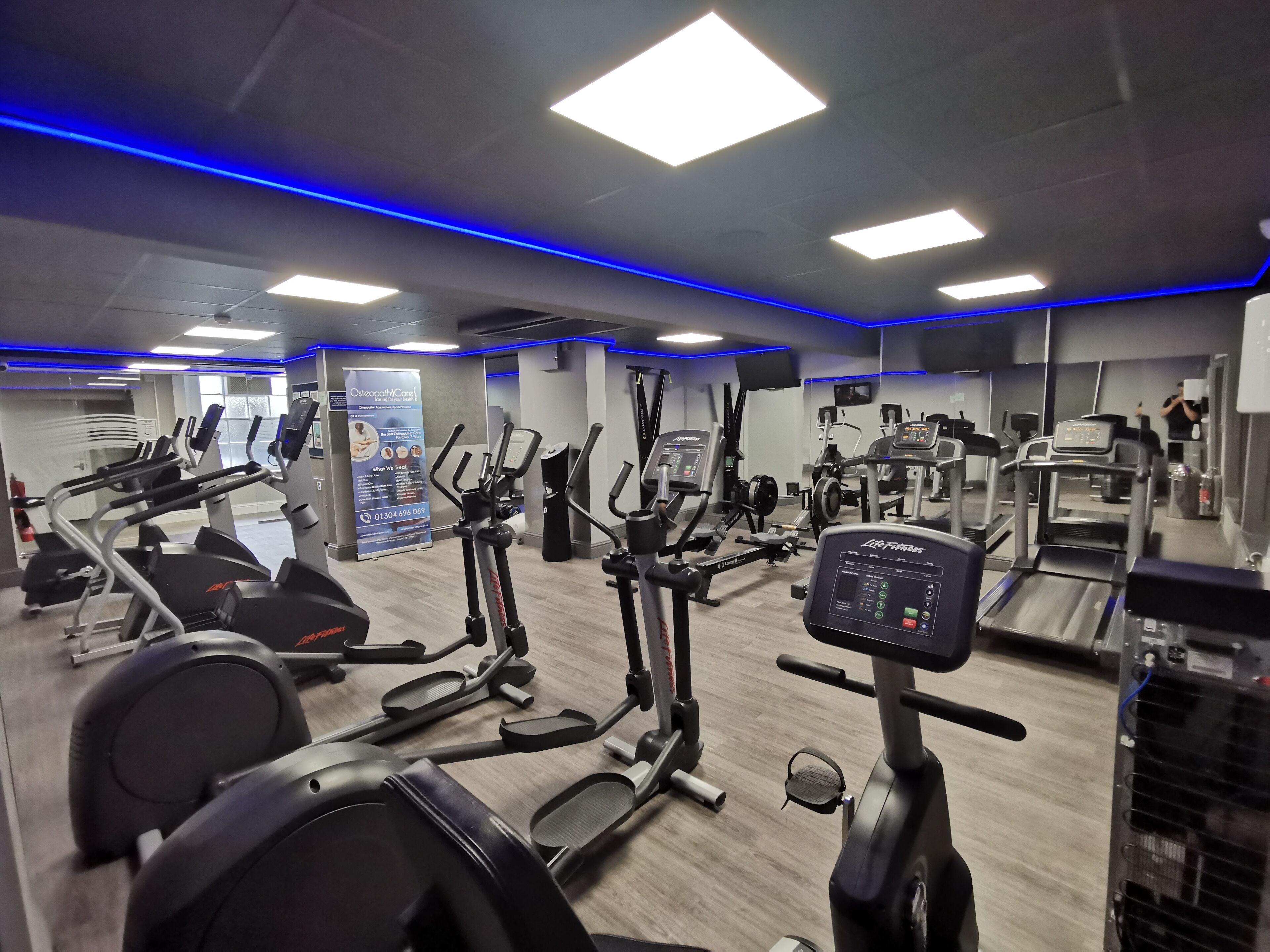 A gym with multiple cardio machines, weight stations, and a mirrored wall.