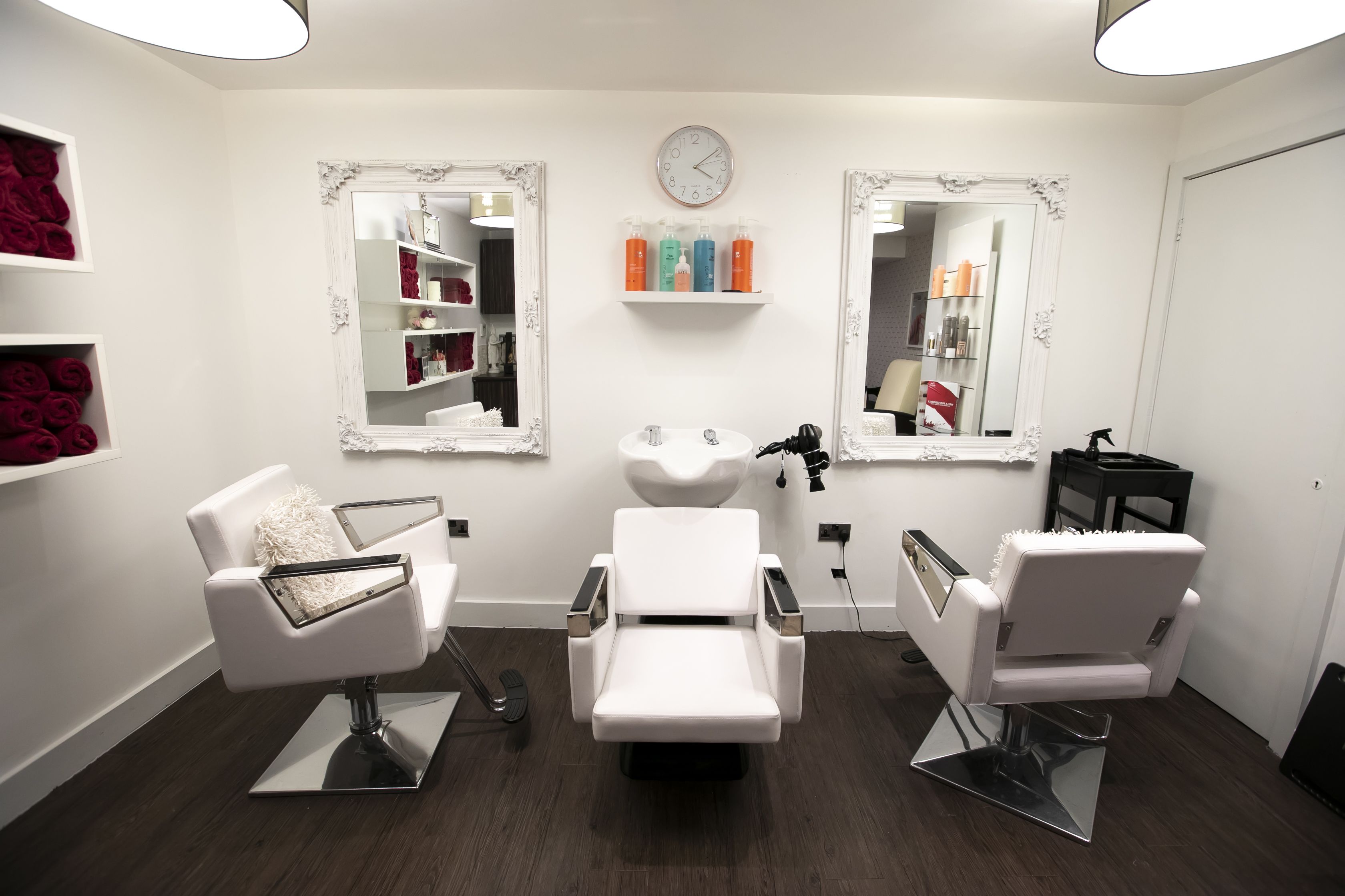A modern salon with three white chairs, a central sink, and mirrors on the walls.