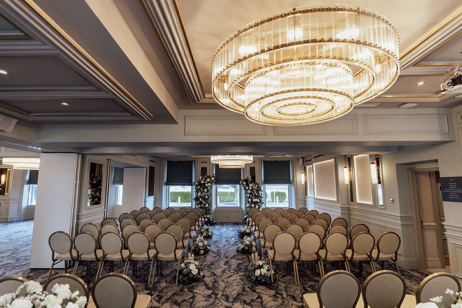 Uma sala de conferências com fileiras de cadeiras, um candelabro e arranjos florais.