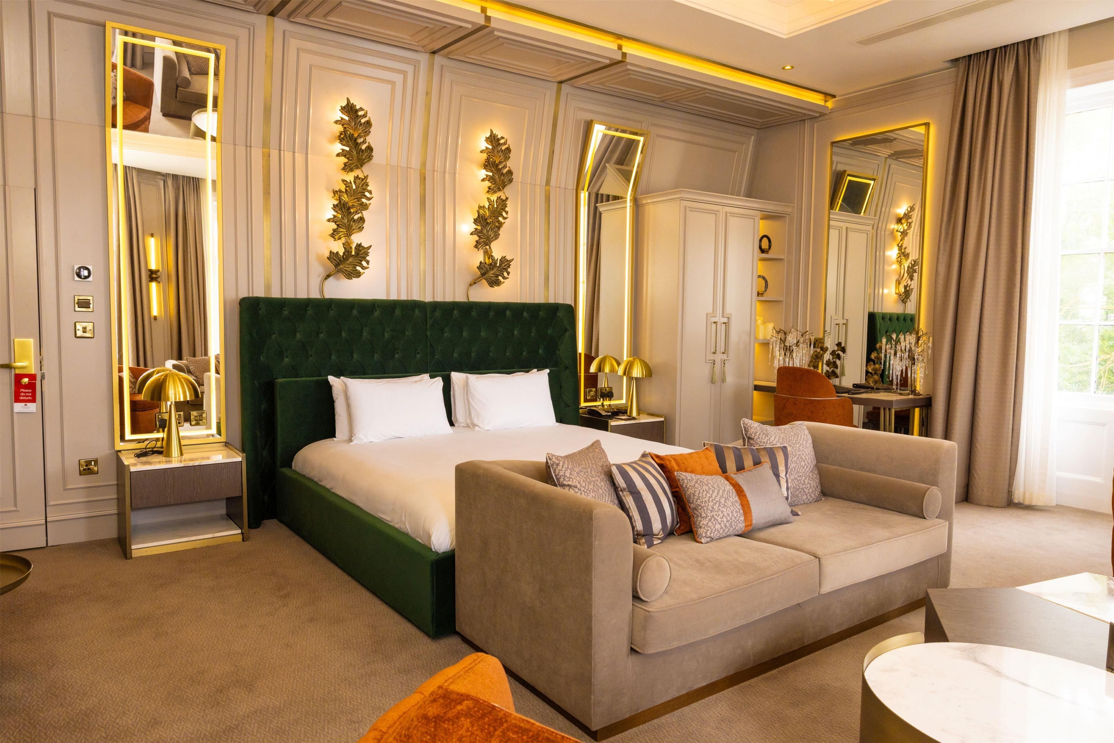 A hotel room with a large bed, a sofa, a desk, and a mirror.