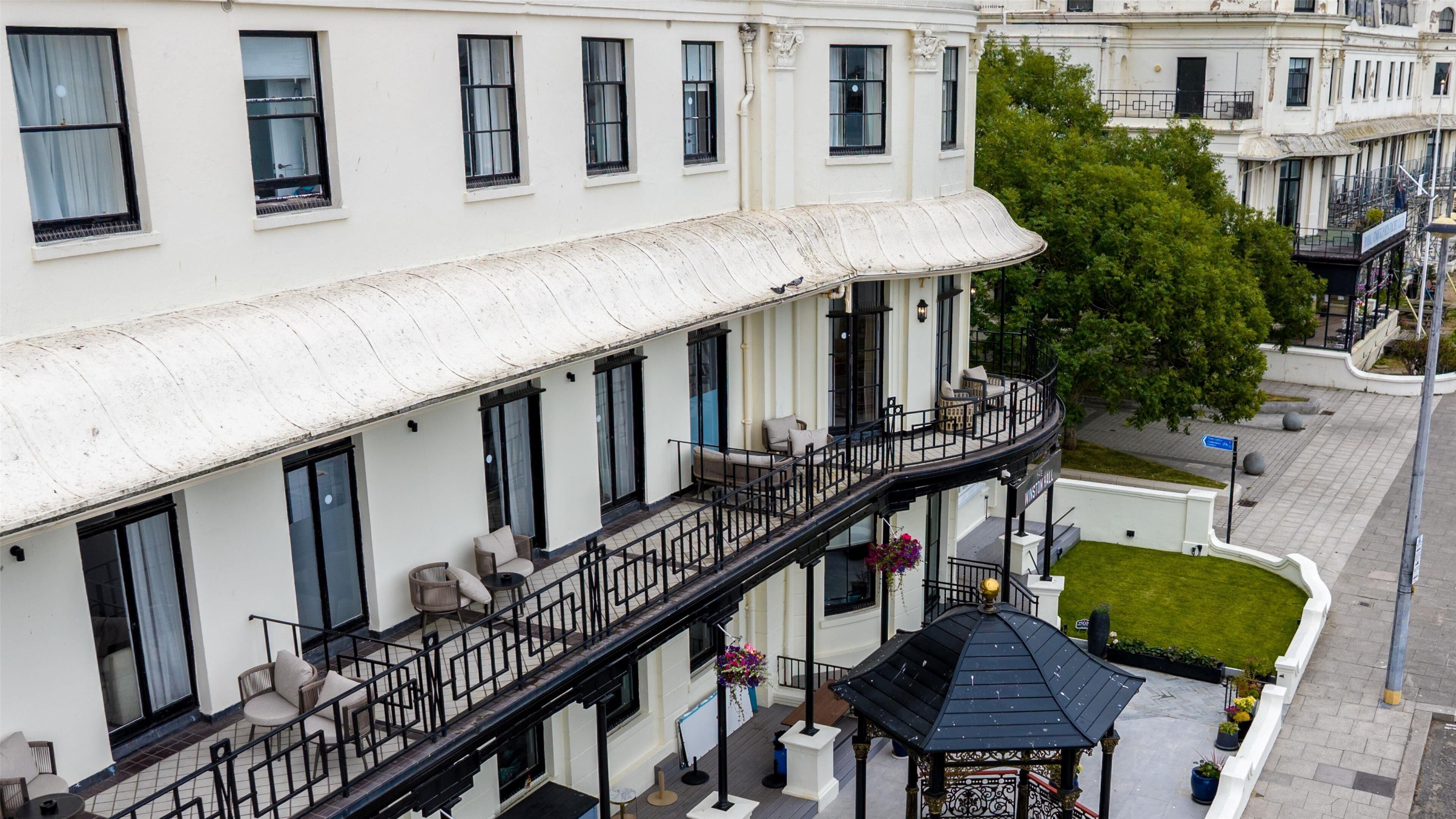 Un edificio de varios pisos con balcones, una zona de estar al aire libre techada y un pequeño pabellón.