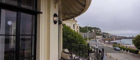 Un balcón con vistas a un pueblo costero, una calle con coches y un edificio con techo curvo.