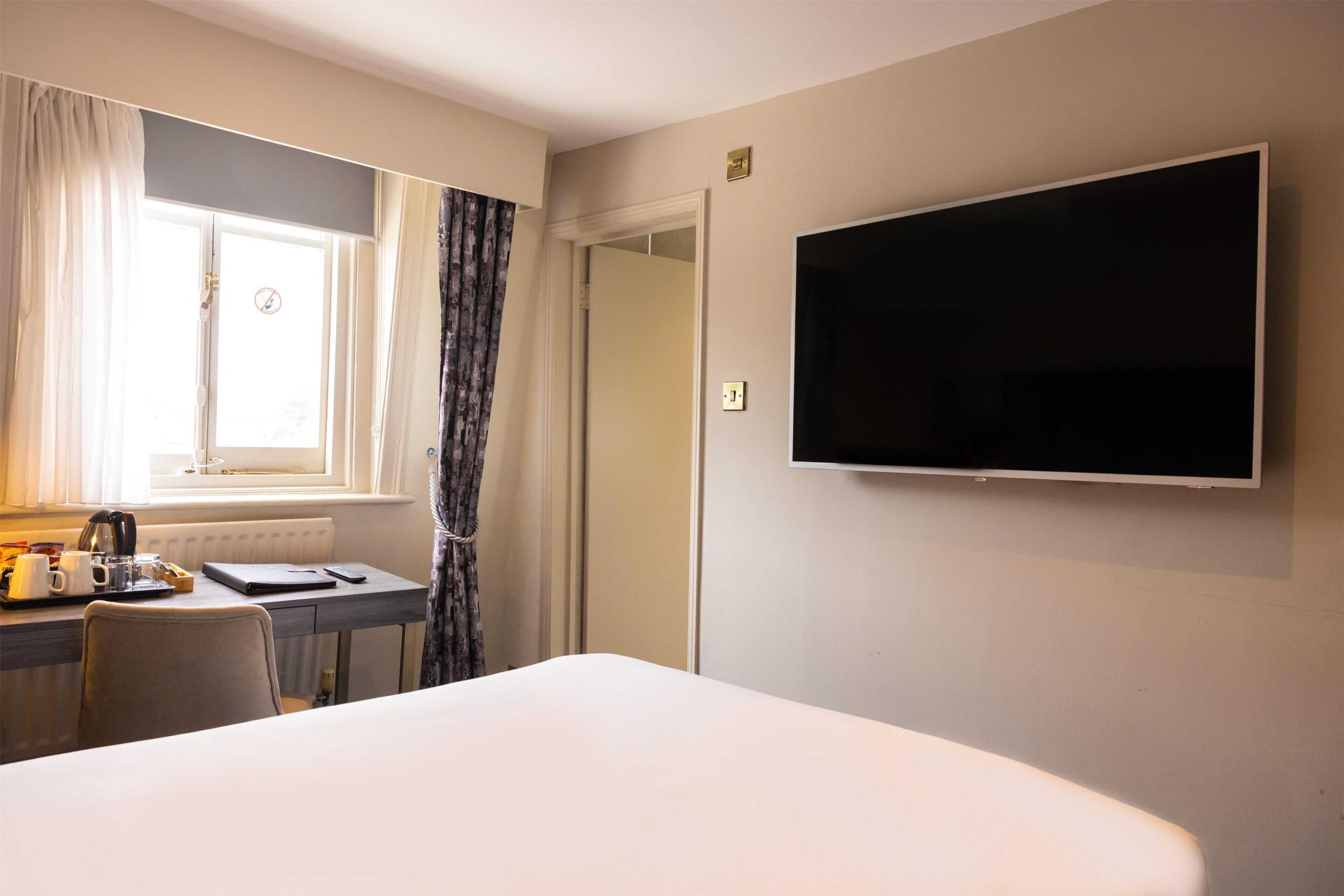 A hotel room with a bed, a desk with a chair, a television, and a window with curtains.