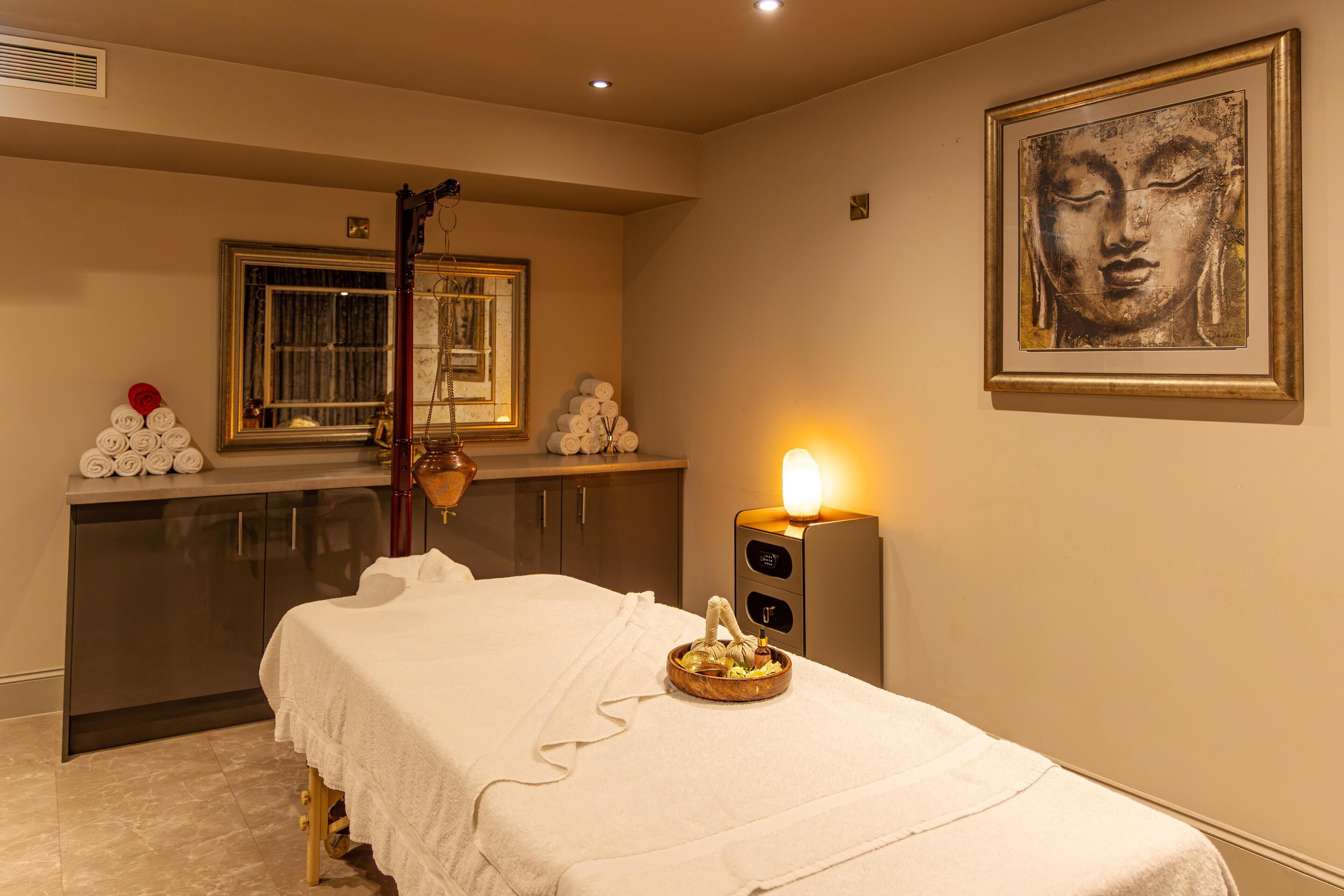 A spa room with a massage table, a wall-mounted heater, a mirror, and a Buddha statue.