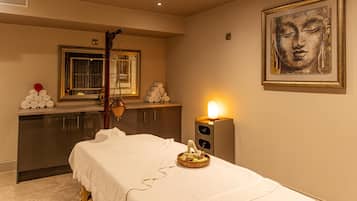 A spa room with a massage table, a wall-mounted heater, a mirror, and a Buddha statue.