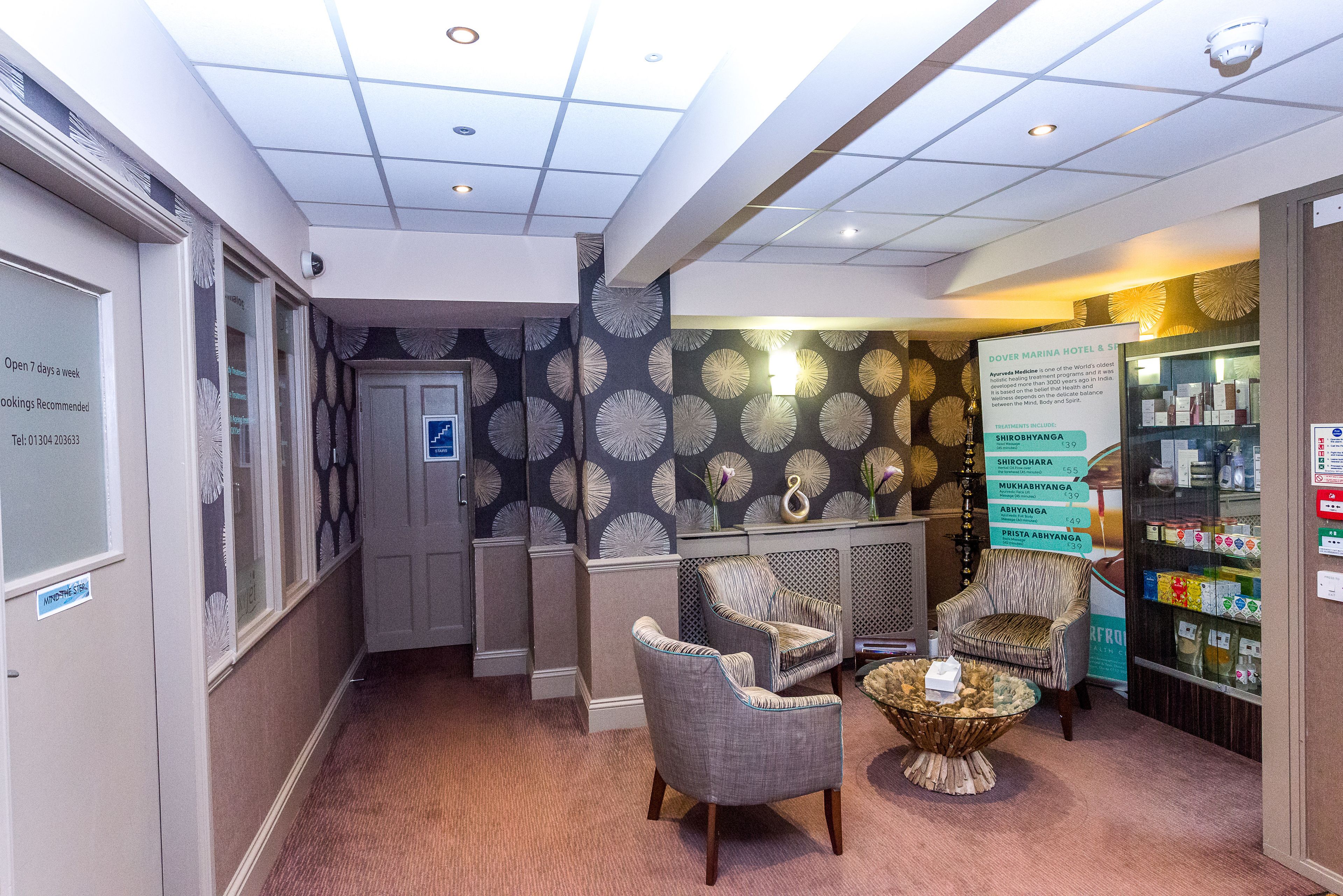 A hotel lobby with a reception desk, two armchairs, a small table, and a wall with a circular pattern.