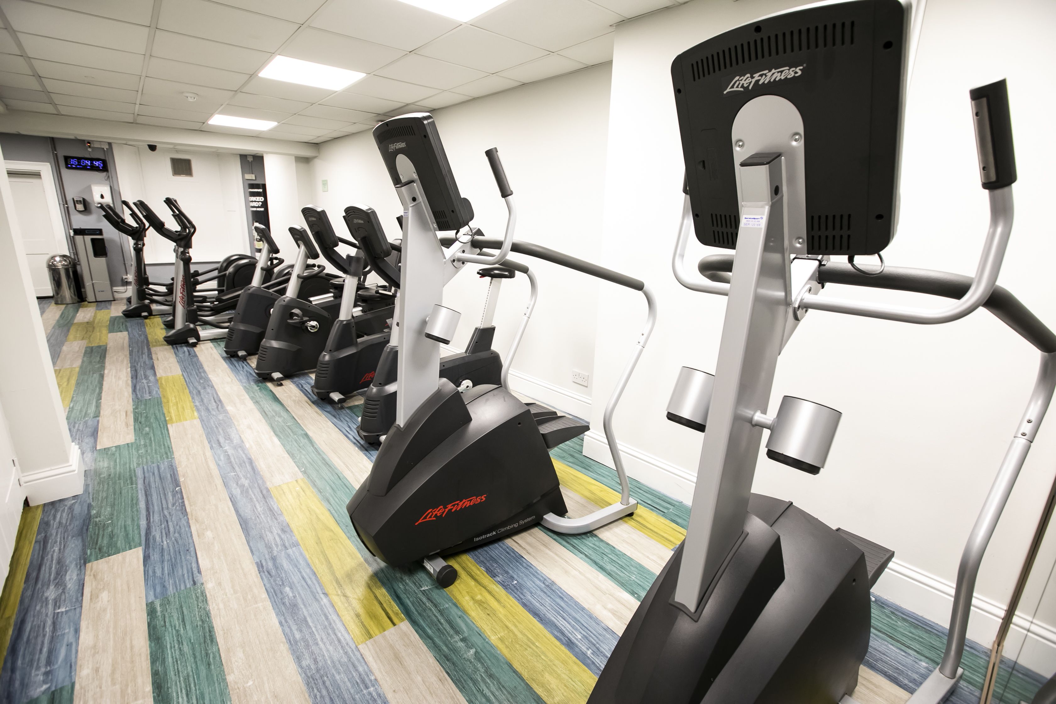 Una palestra con diverse macchine cardio, tra cui tapis roulant ed ellittiche, disposte in fila.
