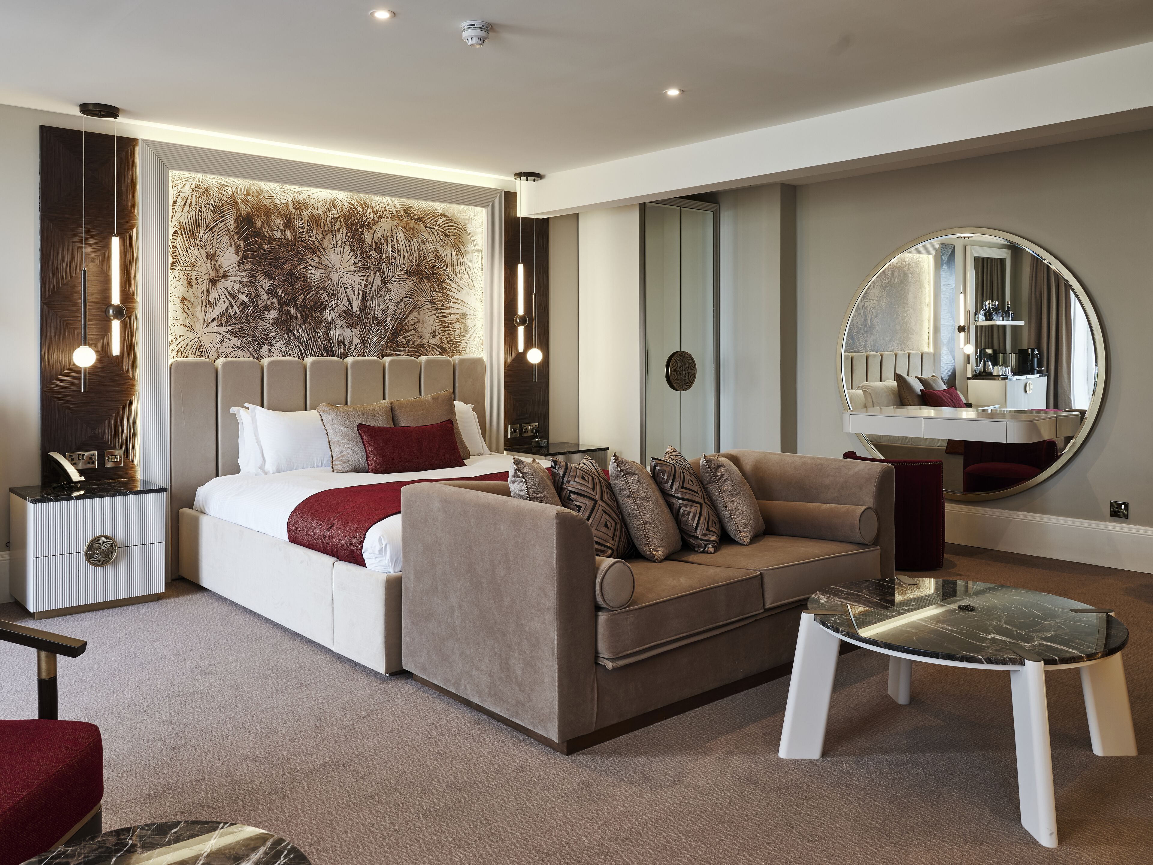 A modern bedroom with a large bed, a sofa, a small table, and a mirror.