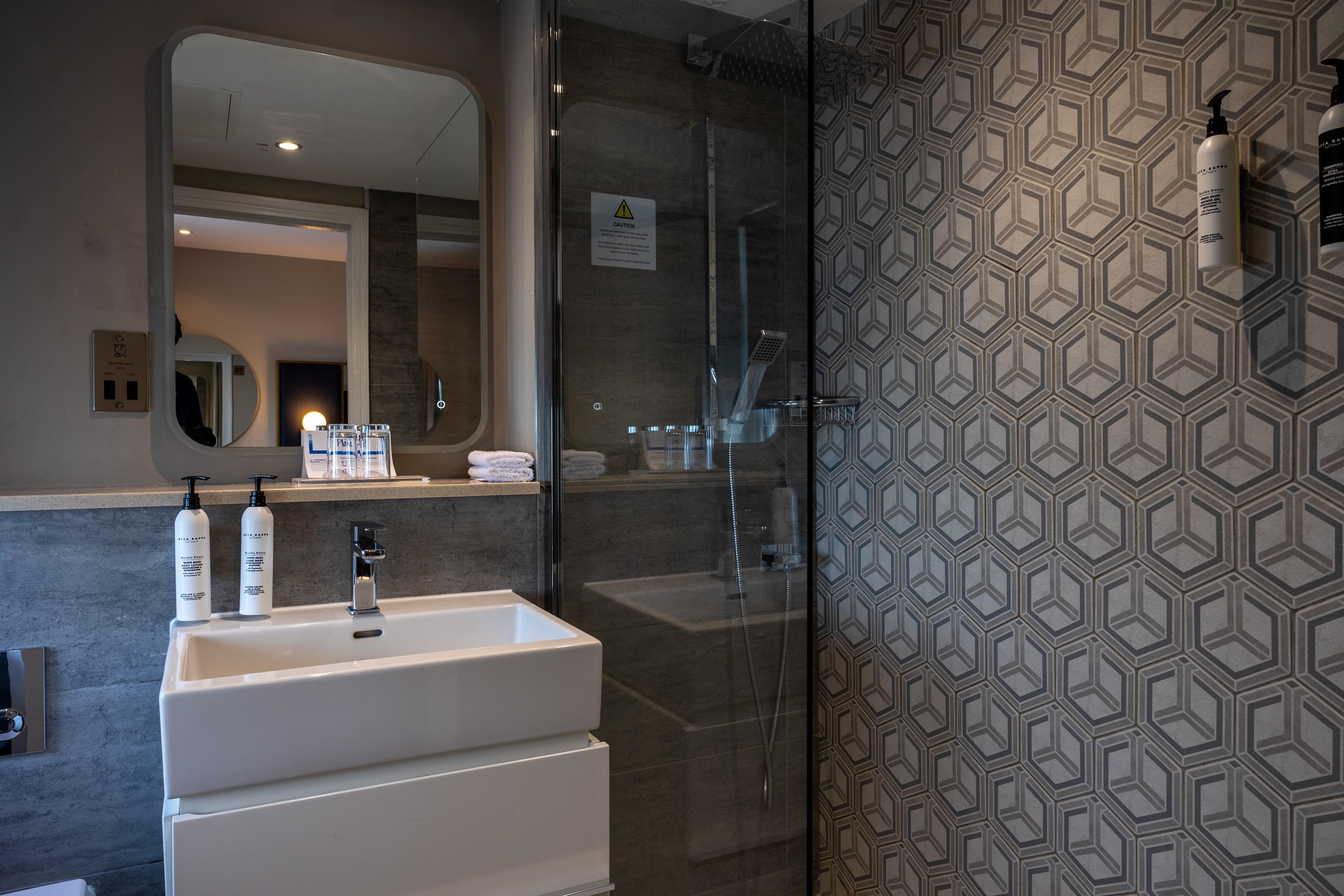 Un baño moderno con cabina de ducha de vidrio, un lavabo blanco y un revestimiento de pared estampado.