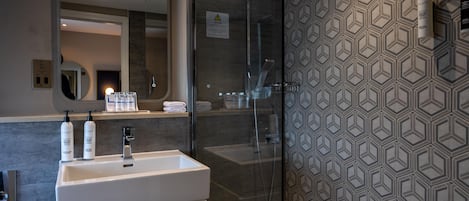 A modern bathroom with a glass shower enclosure, a white sink, and a patterned wall.