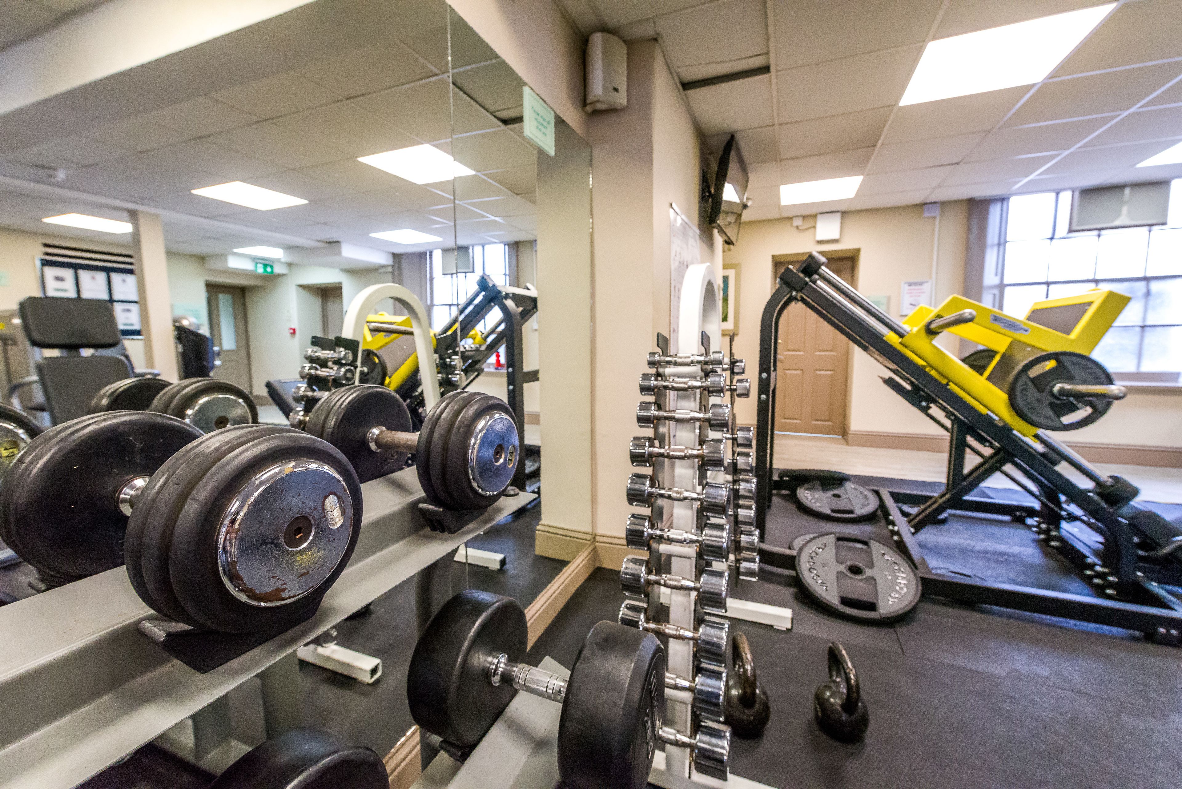Academia com equipamentos de musculação, espelhos e esteira.