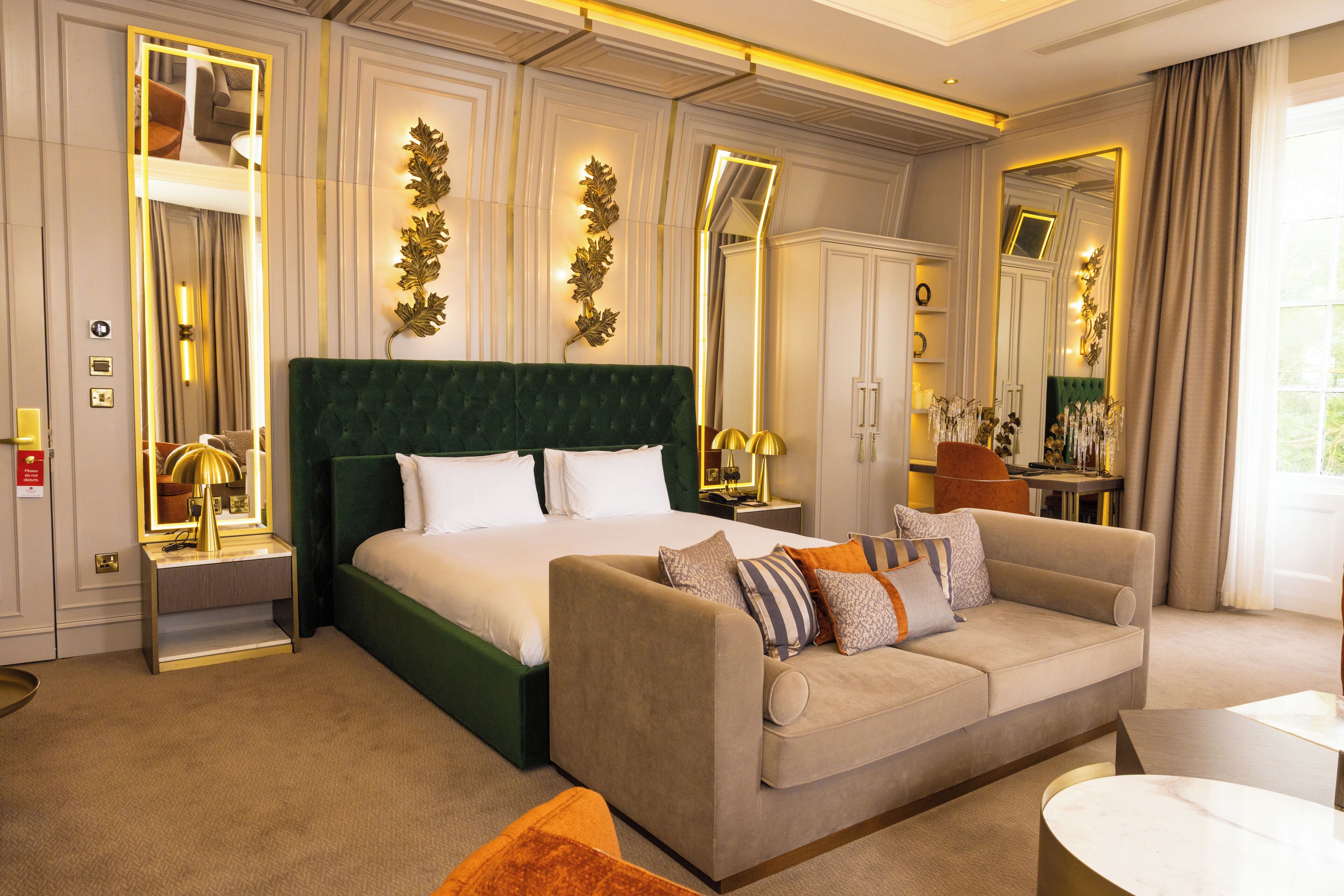 A hotel room with a large bed, a sofa, a desk, and a mirror.