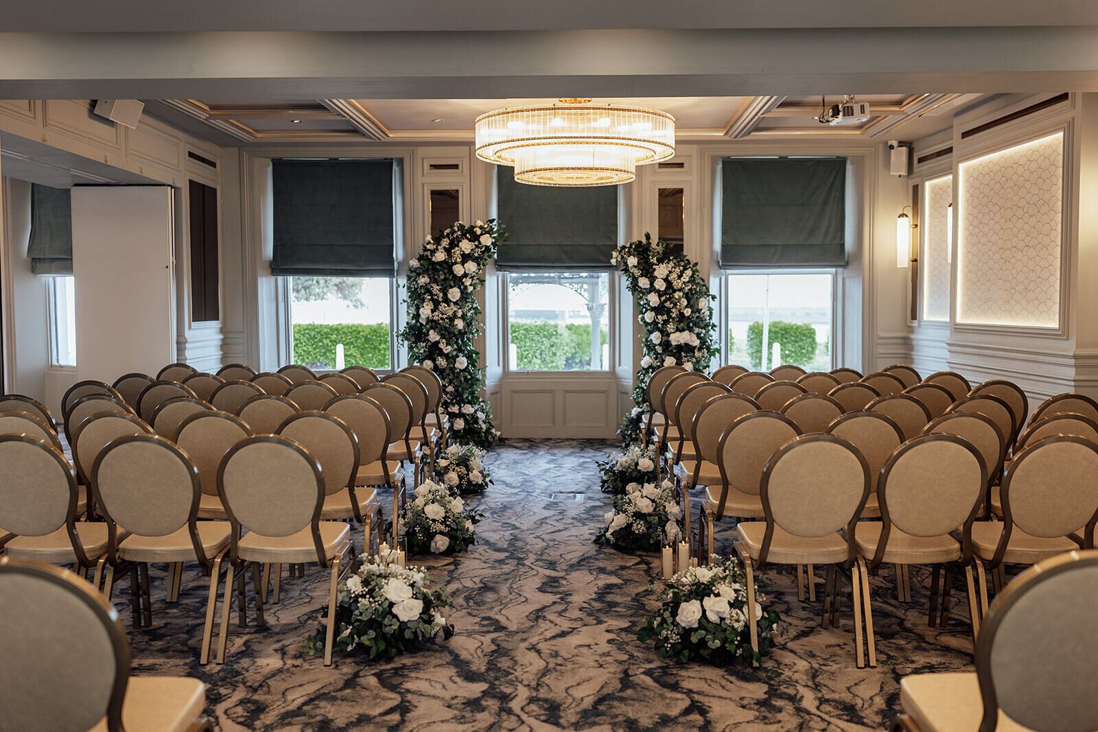 Une salle de conférence avec des rangées de chaises disposées face à une scène, décorée de compositions florales et d’un lustre.