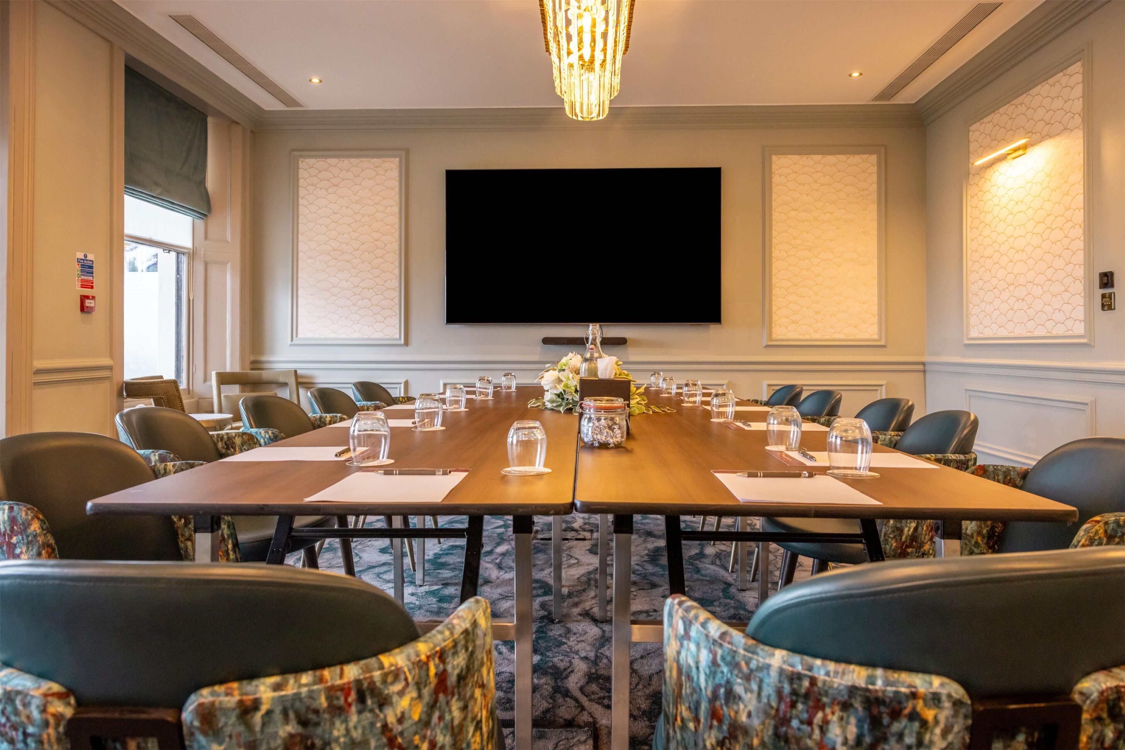 A conference room with a long table, chairs, a chandelier, and a flat-screen TV.