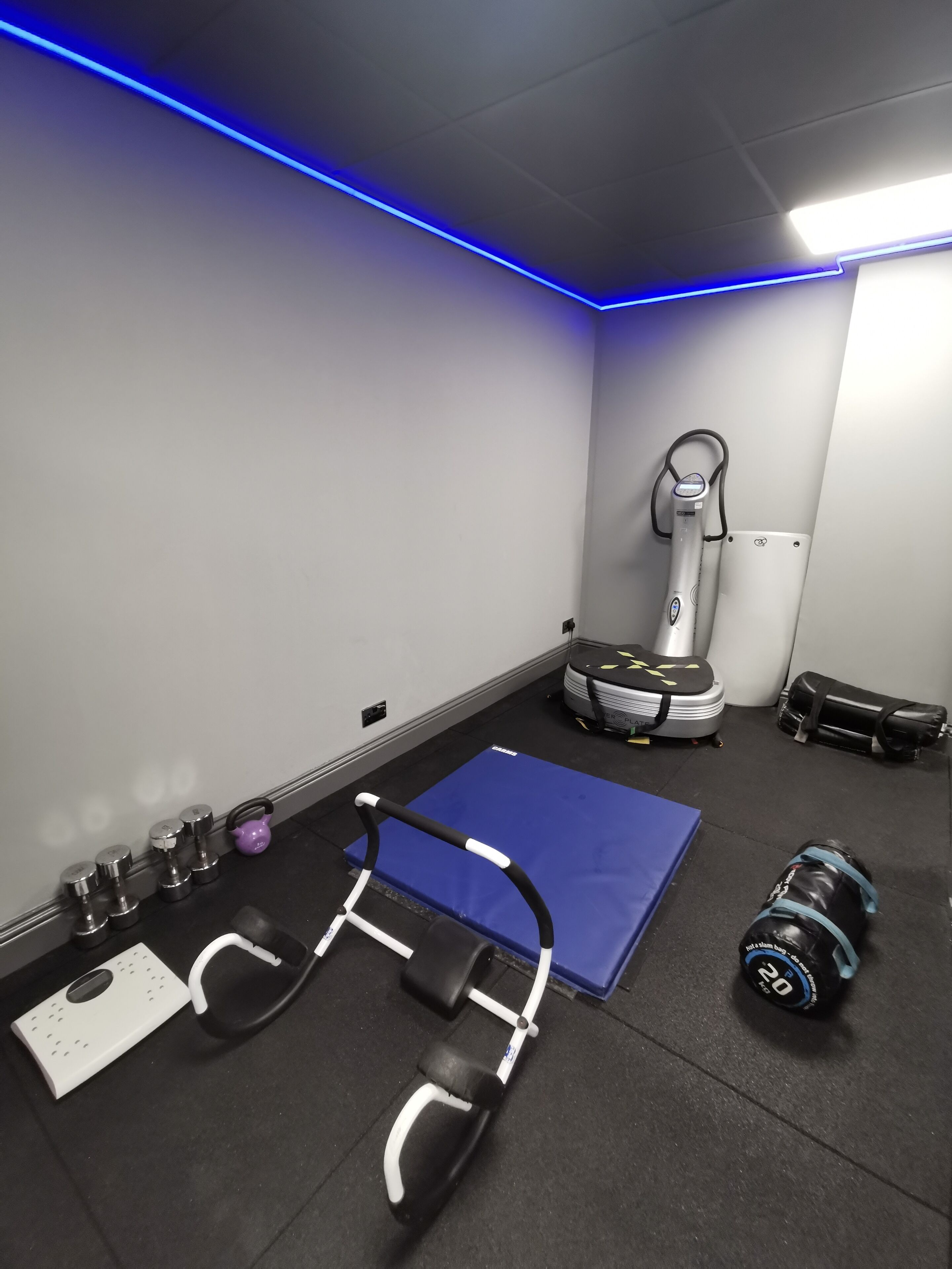 Ett gym med träningsredskap, en blå matta och en taklampa.