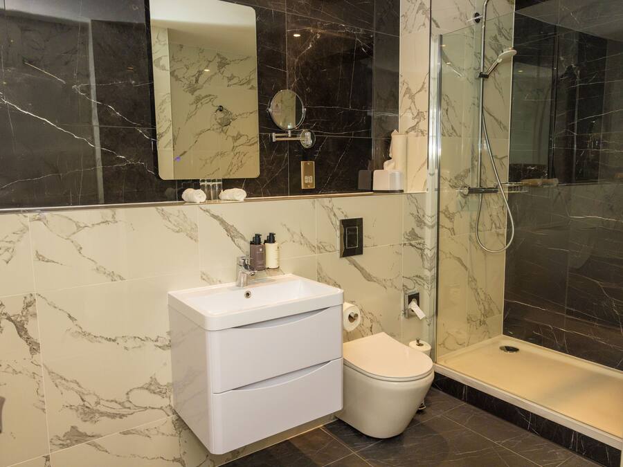 Un baño con tocador de mármol, inodoro y ducha con mampara de vidrio.