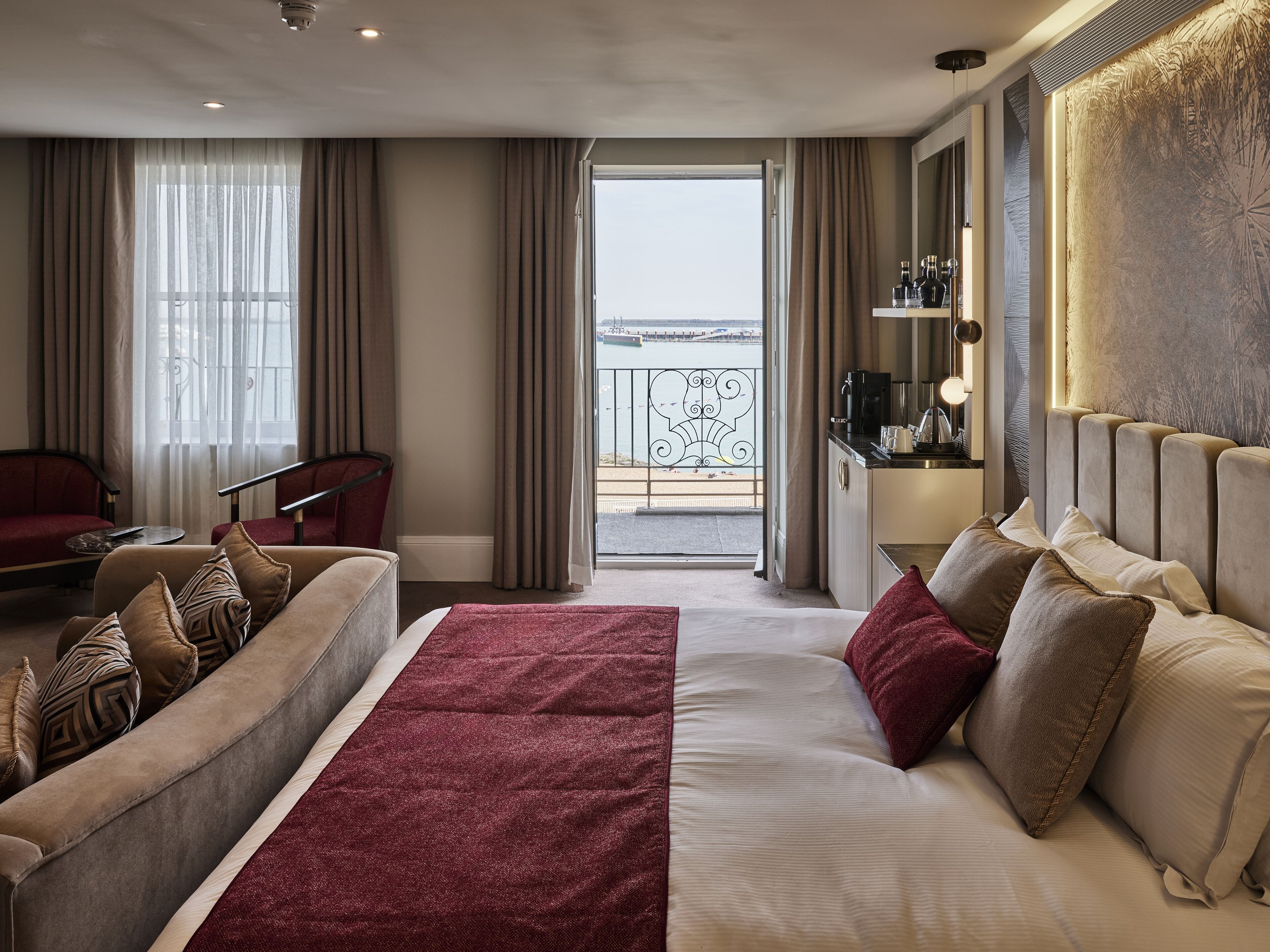 A hotel room with a bed, a sofa, a desk, and a view of the sea.