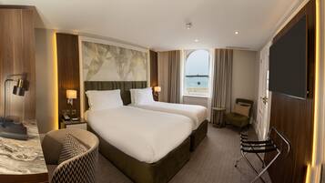 A hotel room with two beds, a desk, a chair, a TV, and a view of the beach.