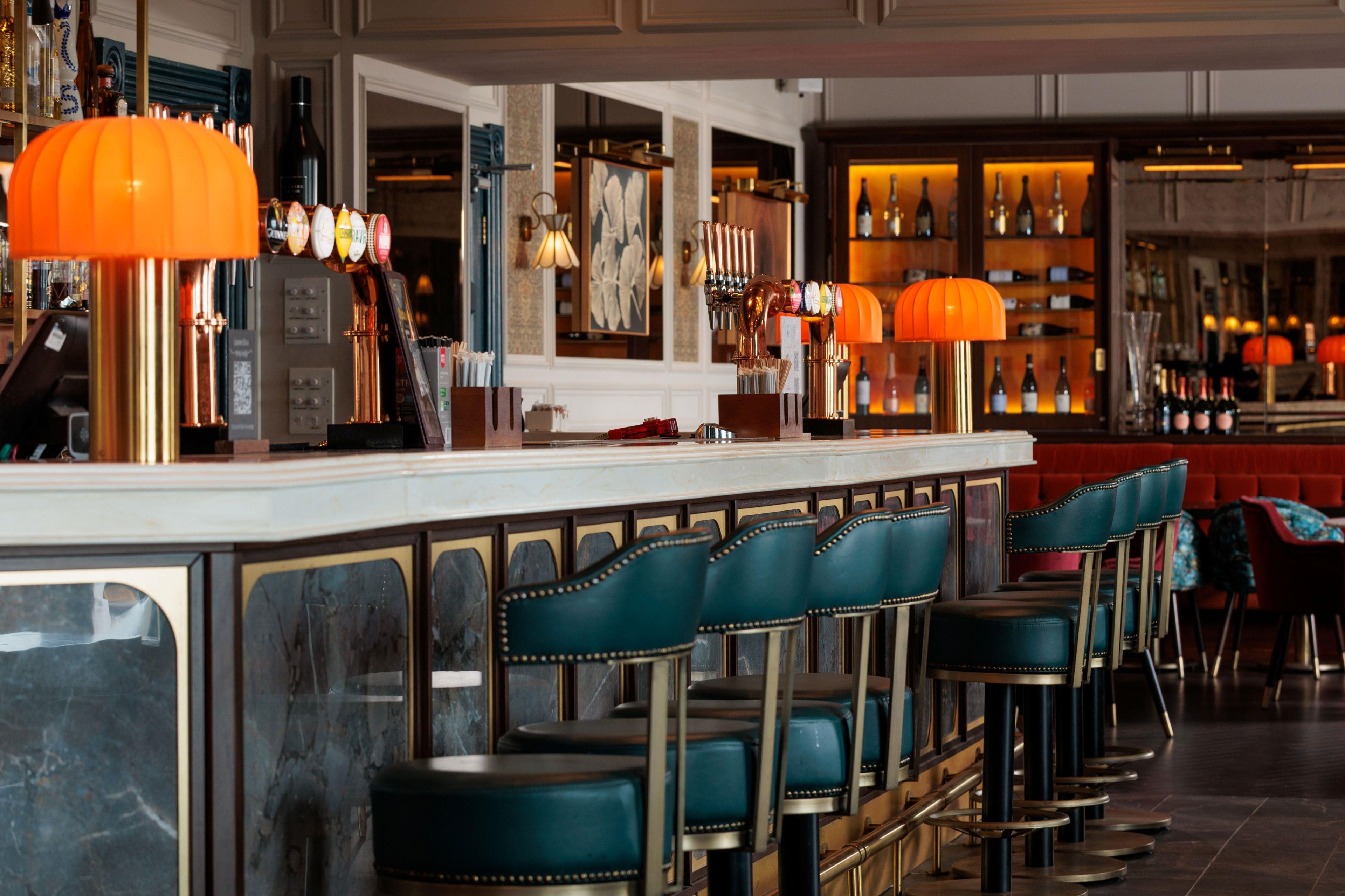 A bar area with a long counter, multiple stools, and overhead lighting.