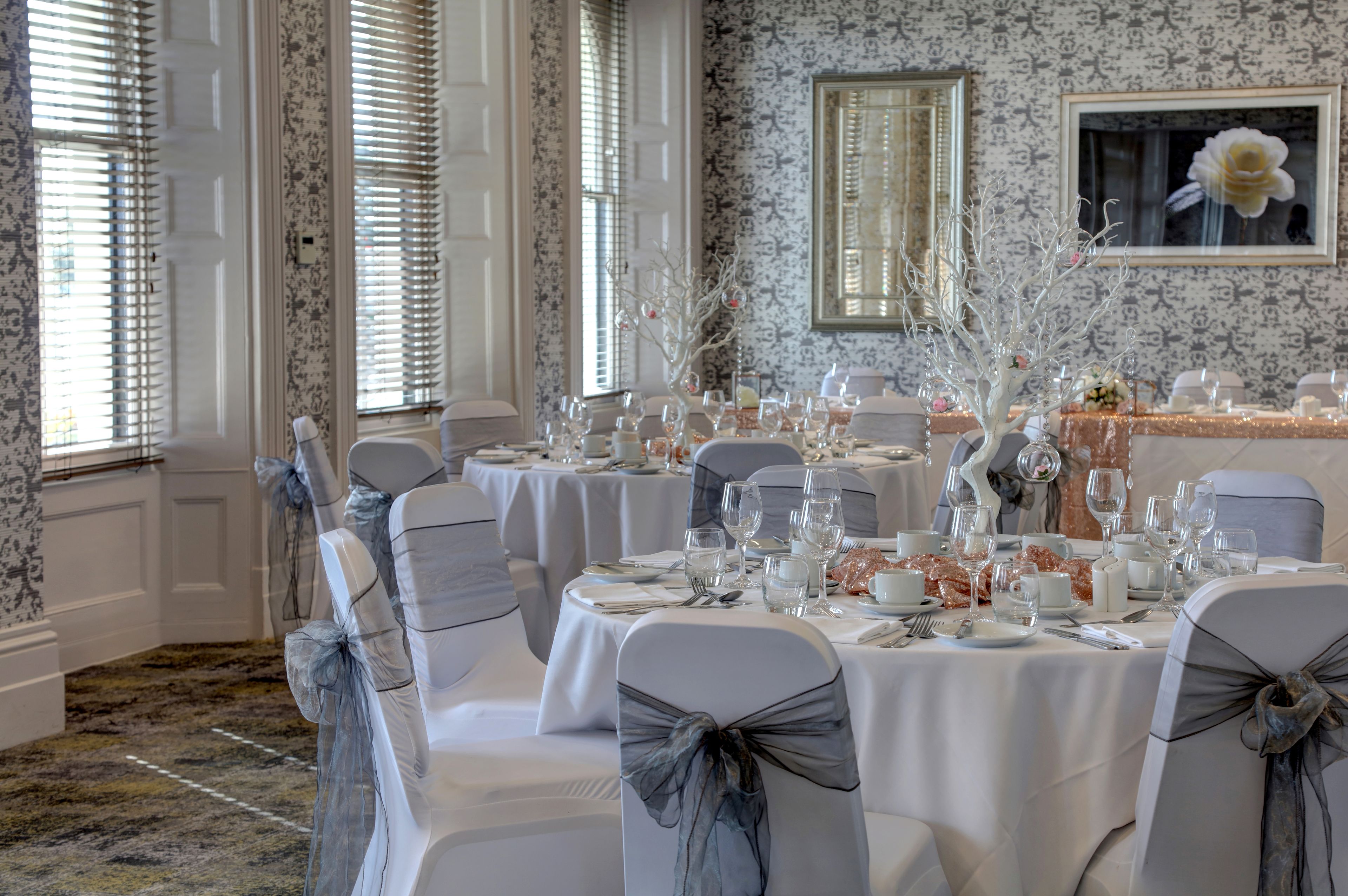 A formal dining room with round tables, white tablecloths, and chairs with grey sashes.