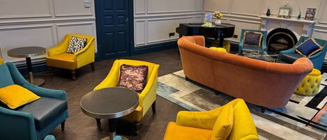 Un área de descanso moderna con una puerta azul, sillones azul y amarillo, una mesa redonda para café y una chimenea decorada.
