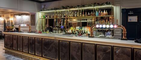 A bar area with a marble counter, shelves of bottles, and a television screen.
