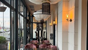 Een restaurantinterieur met grote ramen, een centraal hanglamp en comfortabele zithoeken.